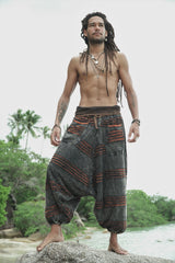Man modelling charcoal stonewashed bohemian razorcut trousers with a rust orange underlayer on tropical beach rocks.