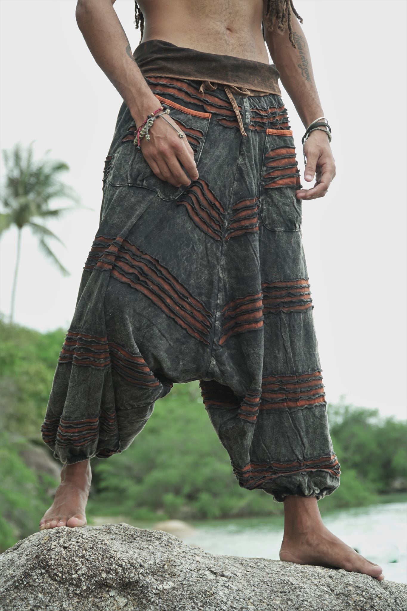View of men's charcoal drop crotch razorcut harem pants where a rust orange underlayer appears under a handcrafted distressed finish.
