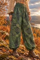 A person outdoors wearing loose, wide-leg patterned pants in lush green with dark abstract motifs, paired with a beige crochet top and brown boots, photographed in an autumn mountain landscape.