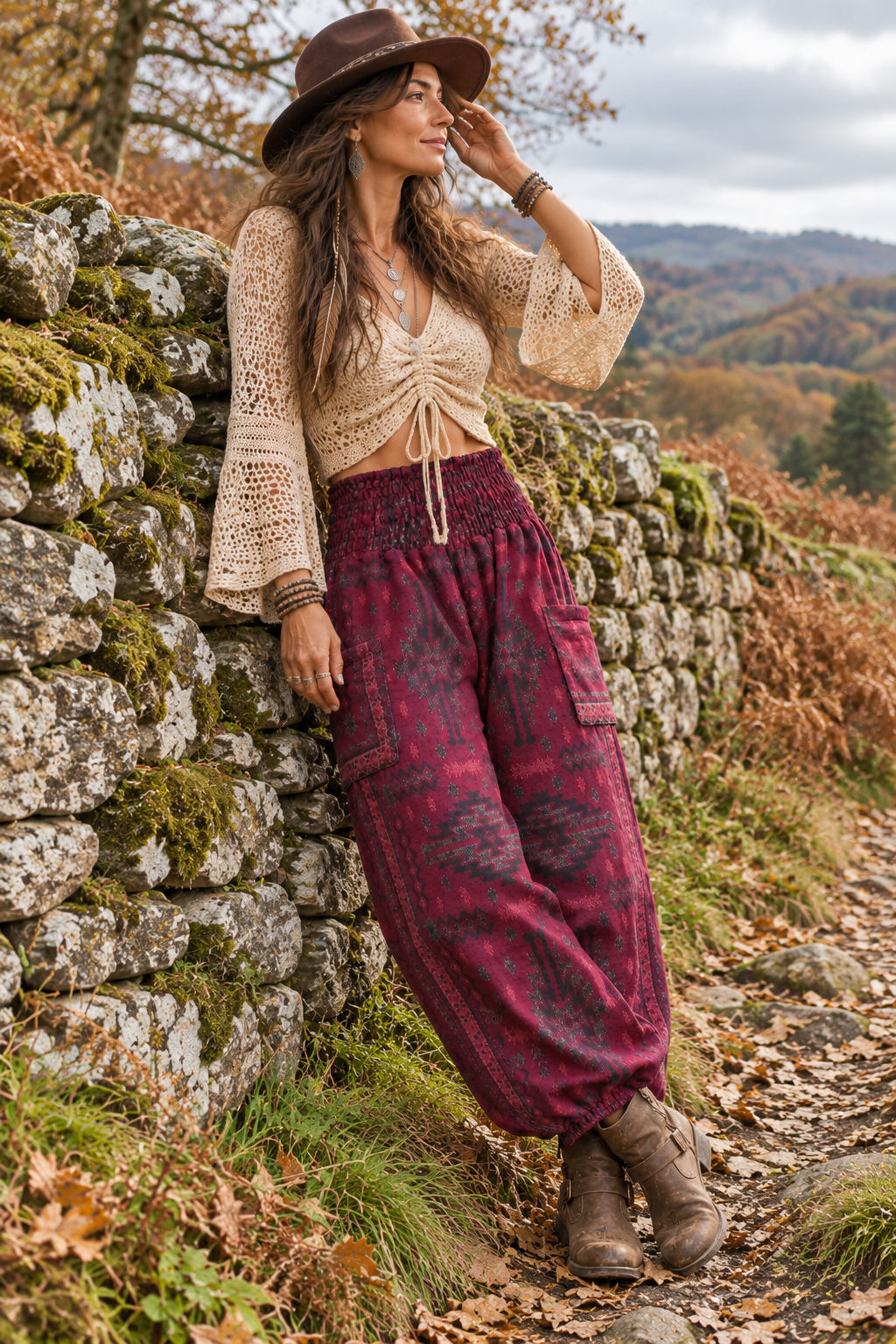 Woman leaning against a stone wall wearing warm maroon boho trousers with a shirred waistband, geometric pattern and low side pockets