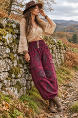 Woman leaning against a stone wall wearing warm maroon boho trousers with a shirred waistband, geometric pattern and low side pockets