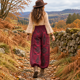 Rear view of woman walking outdoors in warm maroon boho harem pants with a geometric pattern and deep shirred waistband.