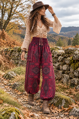 Woman wearing maroon hippie harem trousers with a geometric woven pattern, styled with a cream crochet top and brown boots for autumn.