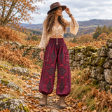 Woman walking outdoors in maroon winter harem pants with a geometric woven pattern, styled with a cream crochet top, hat and brown boots.