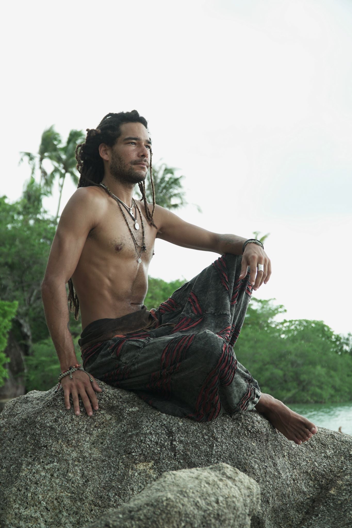 Side profile of a man wearing charcoal grey stonewashed bohemian drop crotch trousers with maroon razorcut detailing and elasticated ankles.