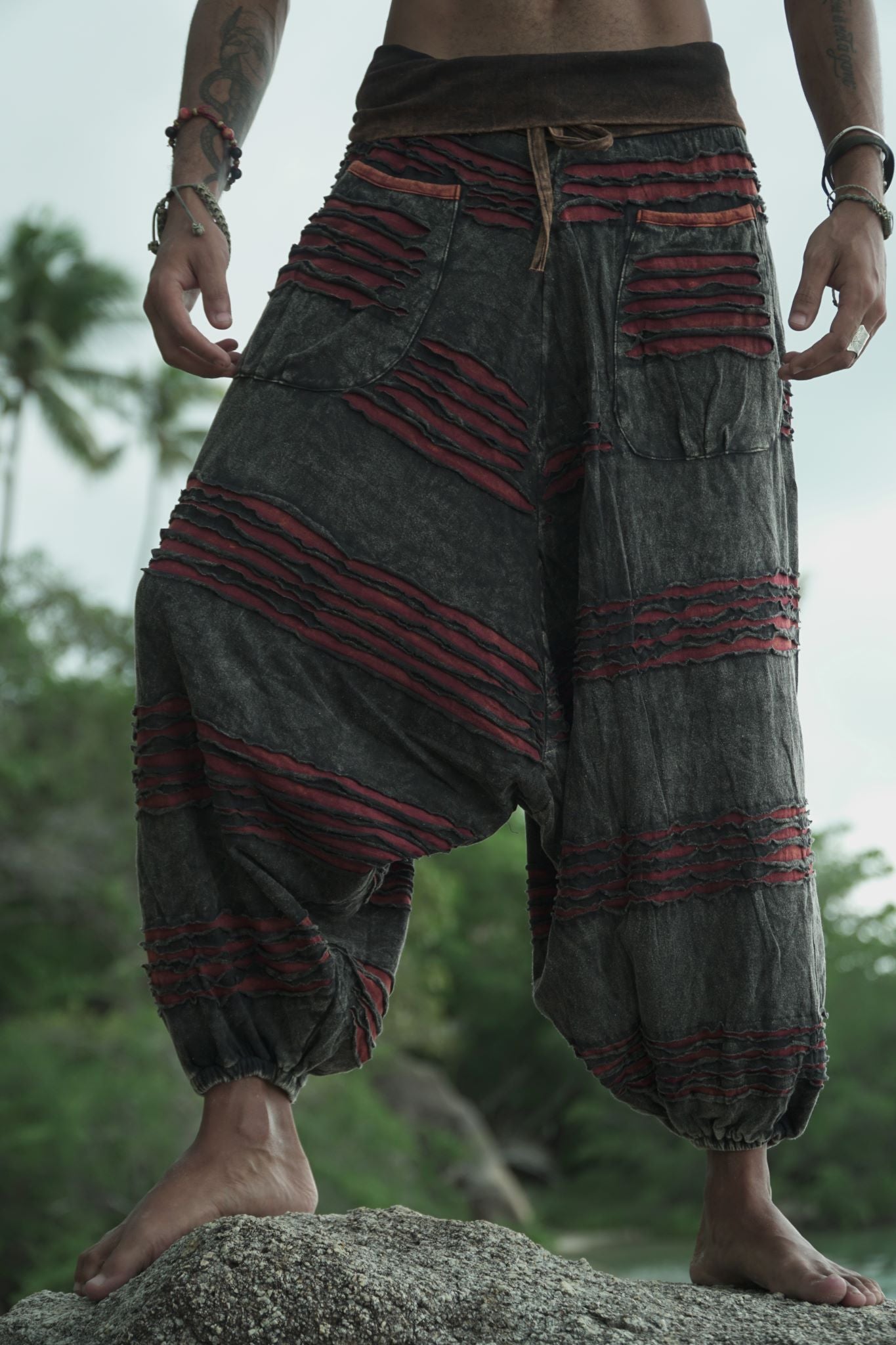 Front view of a man wearing charcoal grey stonewashed drop crotch trousers with a maroon razorcut underlay, elasticated waistband and ankle cuffs.