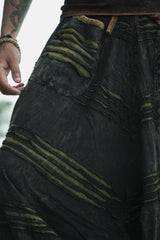 Close-up of men's charcoal grey stonewashed boho trousers showing razorcut pocket detail with a green underlayer and stonewashed fabric on a tattooed male model.