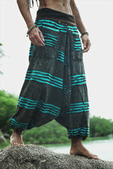 Waist-to-feet hero shot of men's charcoal stonewashed drop crotch  harem trousers with a vivid blue razorcut underlayer, showing oversized pockets, wide leg drape and elasticated ankles on a beach rock.