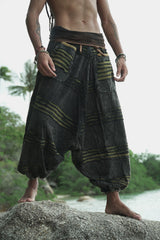 Waist-to-feet view of men's charcoal stonewashed drop crotch trousers with a green razorcut underlayer, showing oversized pockets, elasticated ankles and relaxed fit on a tropical beach rock.