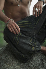 Close-up of charcoal stonewashed men's harem pants showing the handcrafted razorcut design with green underlayer detail and textured cotton fabric, worn cross-legged on a rock.