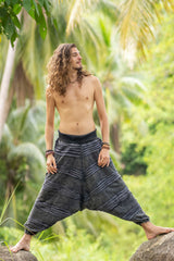Man modelling grey stonewashed cotton razorcut boho trousers with a relaxed drop crotch fit, layered razorcut panels and elasticated cuffs in a tropical setting.