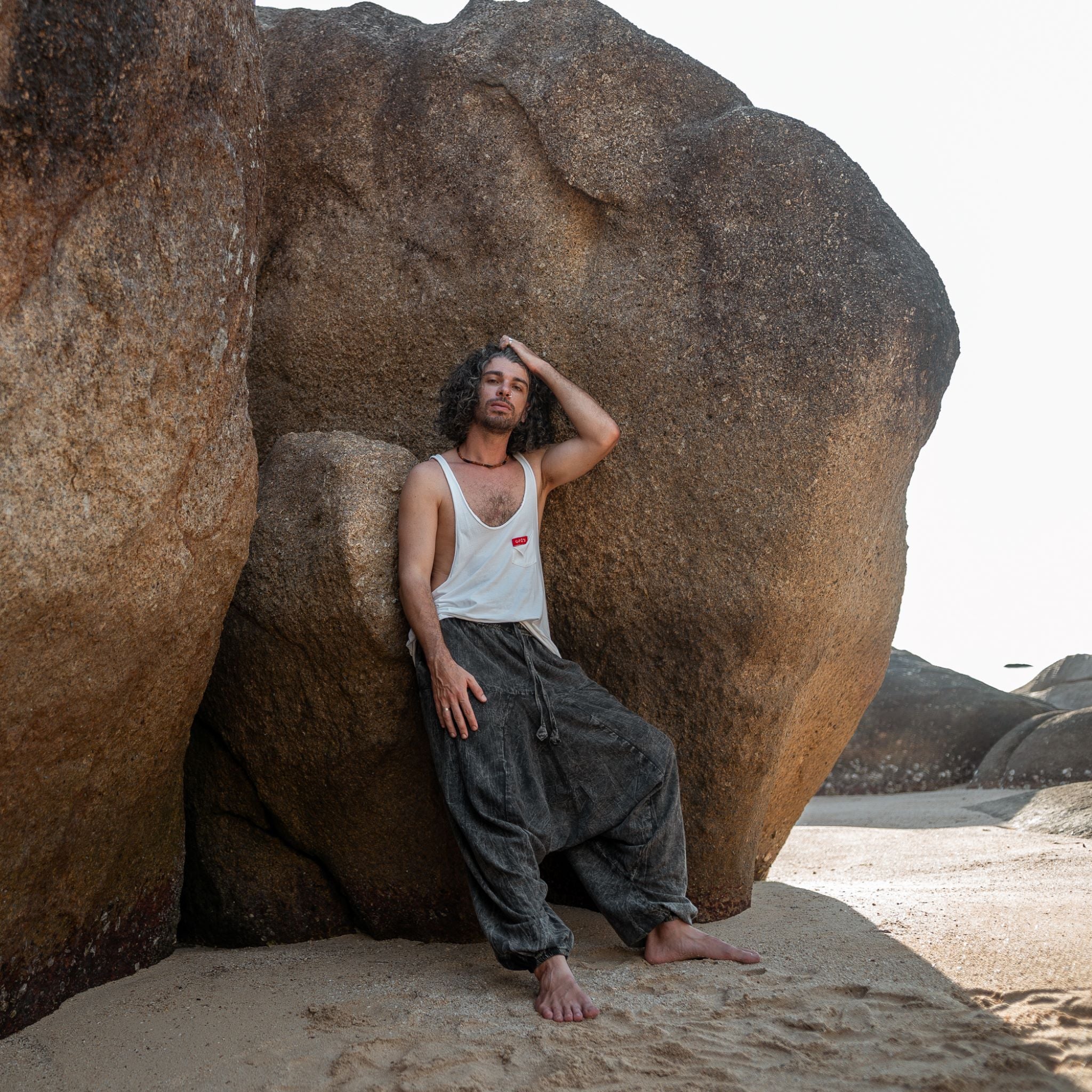 an leaning against rock wearing charcoal grey stonewashed drop crotch harem pants, boho festival style