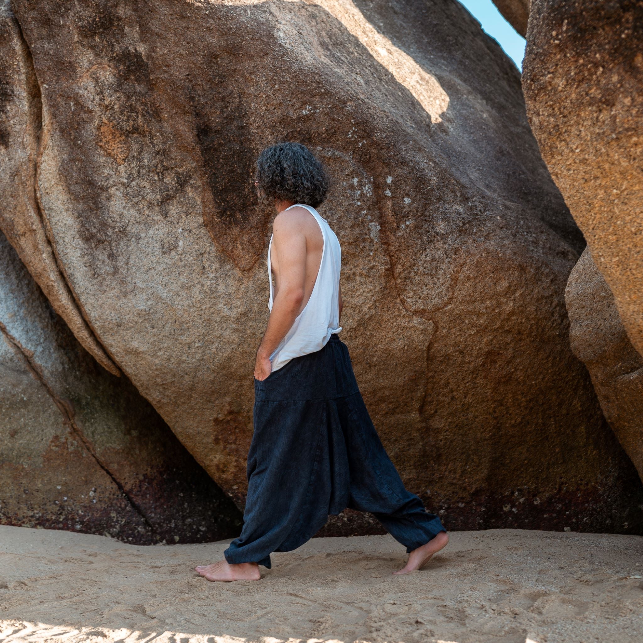 Man walking barefoot on beach wearing navy stonewashed drop crotch harem pants, boho festival style