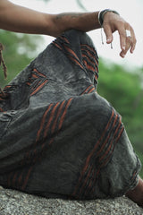 Close-up of men's charcoal stonewashed razorcut harem pants with a rust orange cotton underlayer, showing handcrafted distressed detailing.