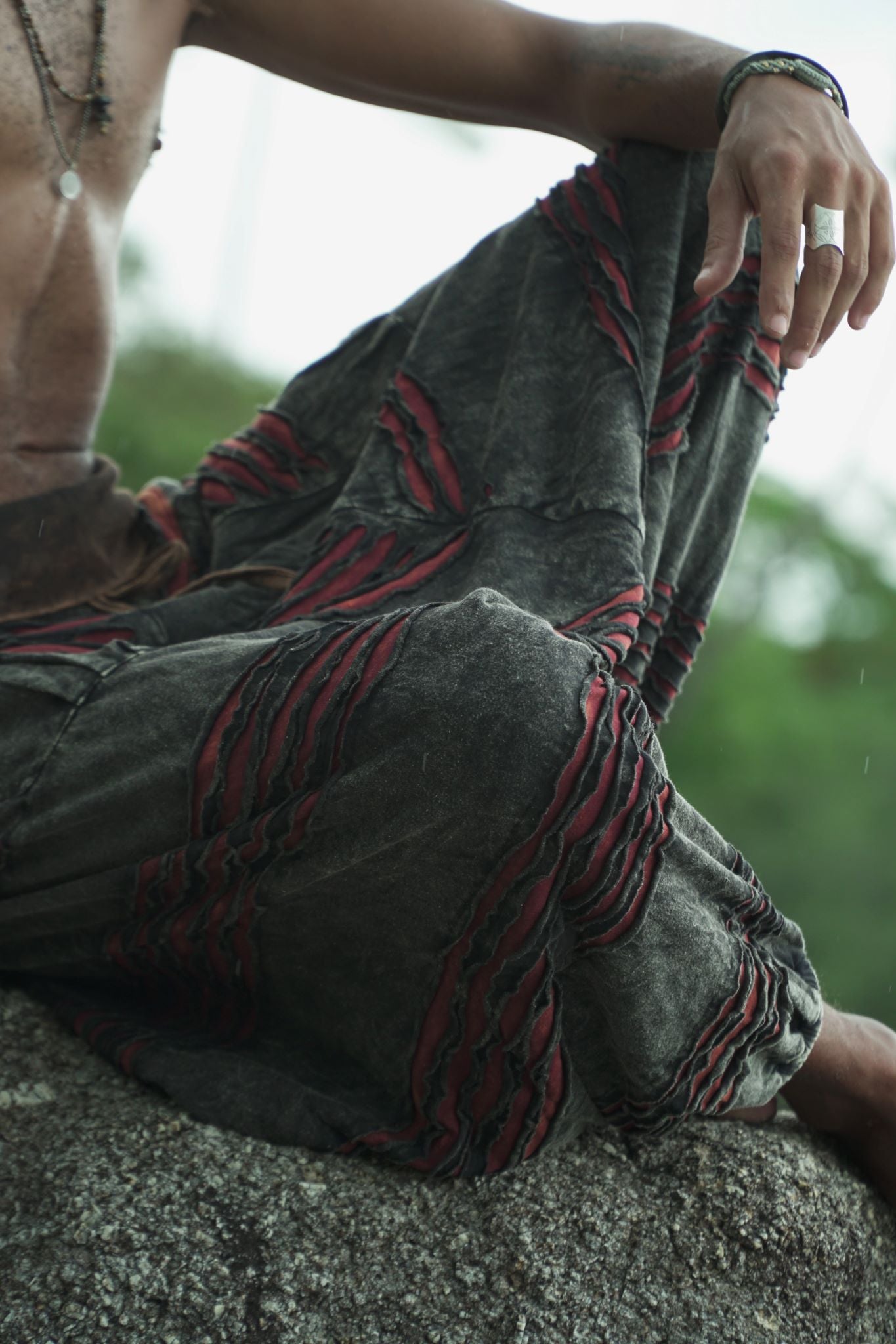 Close-up of men's stonewashed razorcut harem pants in charcoal grey with a maroon underlay, showing handcrafted layered razorcut detailing and relaxed cotton fabric.