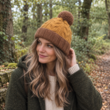 Close-up of mustard and brown chunky knit wool hat showing the cable-knit texture, brown ribbed upturned rim