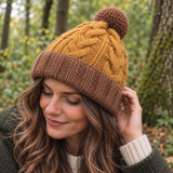 Woman wearing a mustard and brown chunky cable knit wool hat with pom pom, made from 100% New Zealand wool and lined with fleece for autumn and winter.