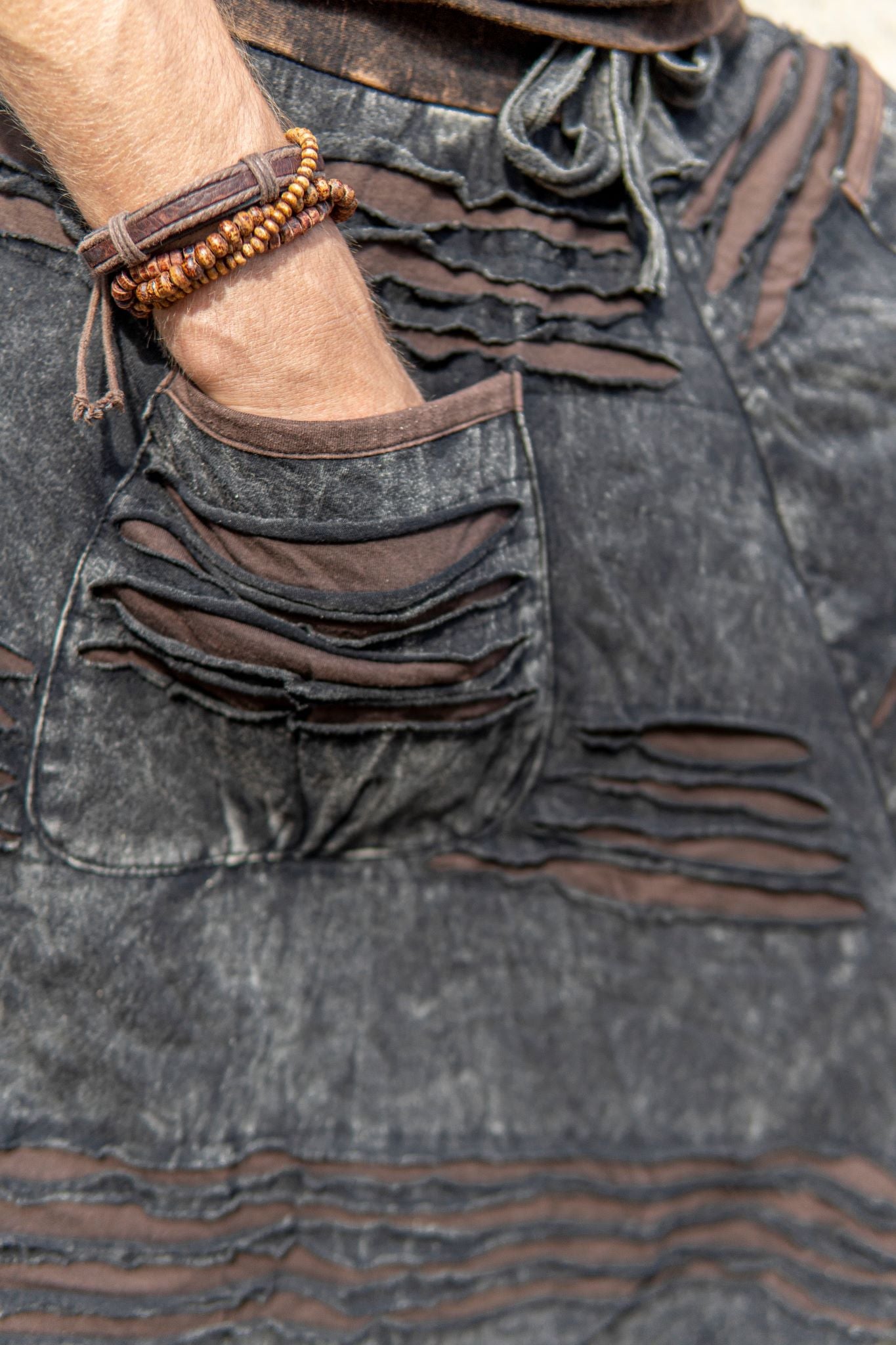 Close-up of charcoal grey stonewashed hippie trousers showing handcrafted razorcut pocket detailing with a brown cotton underlayer.