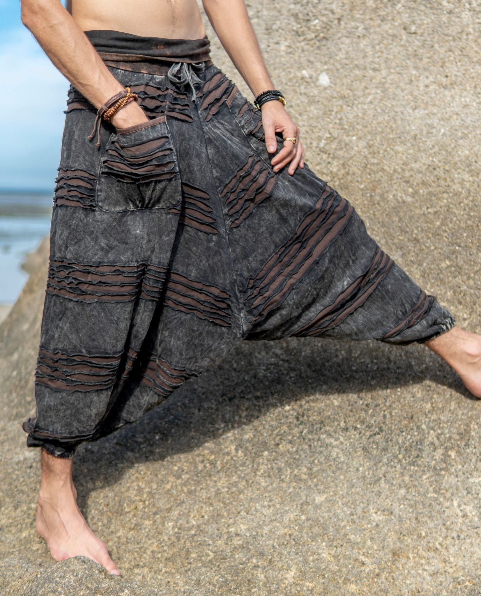Men's charcoal grey stonewashed razorcut harem pants with a brown underlay, styled in a relaxed tropical beach setting.underlayer.