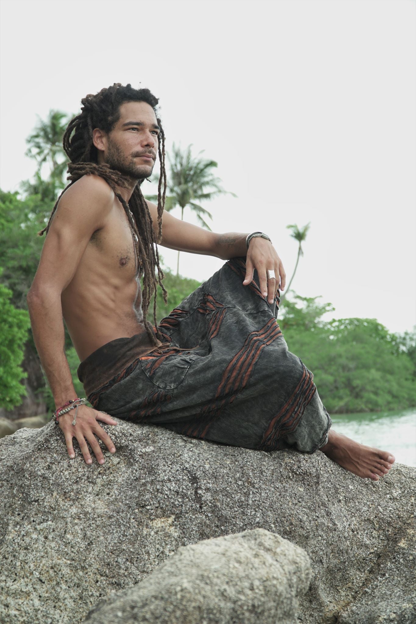 Side view of men's charcoal stonewashed razorcut harem pants with a rust orange underlayer, photographed outdoors.