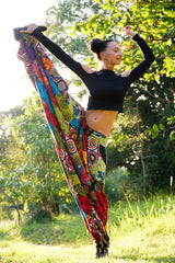 Women's colourful patchwork harem pants demonstrating flexibility with high kick pose, showing wide leg fabric flow outdoors